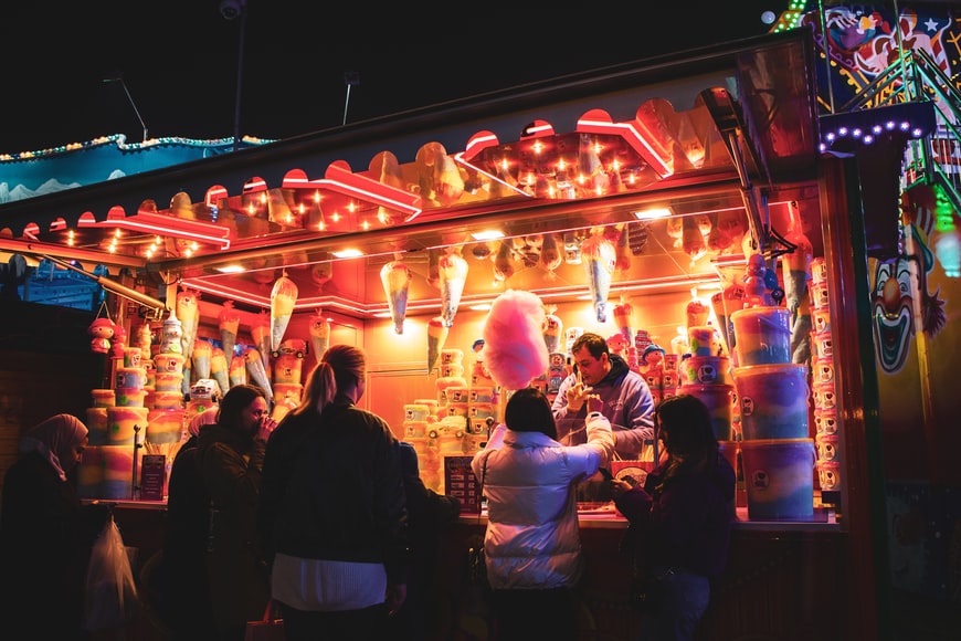 a family buys cotton candy from a cotton candy vendor at a christmas market. the lighting is warm and festive. clooper, clooper app